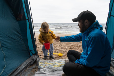 Dad and baby are playing together in a tent on the seashore. The concept of adventure, family camping, outdoor activities, bonding.の写真素材