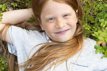 Portrait of a red-haired boy with long hair on the grass. Flat lay.The happy boy smiles. Copy space.