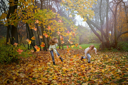 Children in the autumn park run, jump, and play among the colorful bright maple foliage. Autumn...
