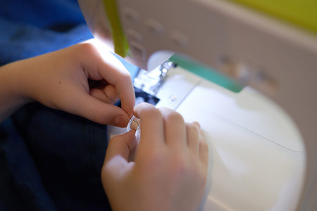 The hands of a young girl who sews on a sewing machine. The concept of small business, hobby, home...