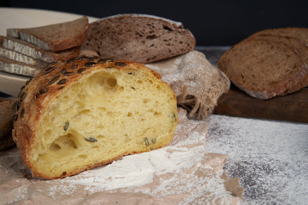 Different types of sliced bread and a loaf on a wooden background . Spilled flour. Front view. Copy...