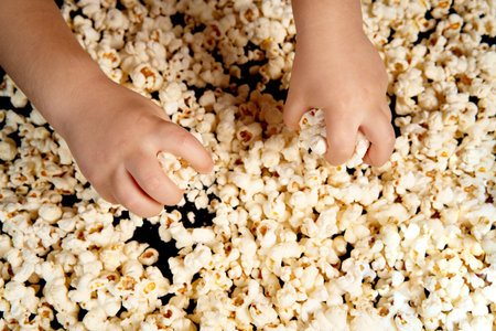 Childrens hands are picking up popcorn. Flat lay . The concept of a birthday, party, holiday, home leisure. Copy space for your product. Popcorn texture or background.の写真素材