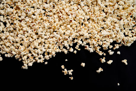 Scattered crispy popcorn on a black isolated background. View from above. The concept of a party and a movie. Copy Space.の写真素材