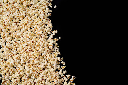 Scattered crispy popcorn on a black isolated background. View from above. The concept of a party and a movie. Copy Space.の写真素材