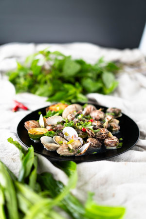 Freshly prepared clams and mussels with garlic served on a black plate, garnished with green herbs.Vertical photo.の写真素材