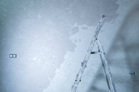 A ladder is positioned against a wall as adhesive is applied to repair surface damage.の写真素材