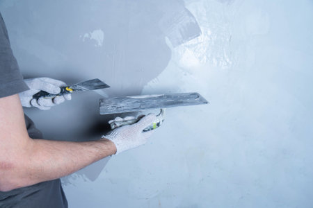 A person applies microcement to a wall surface with a putty knife in a workshop.の写真素材