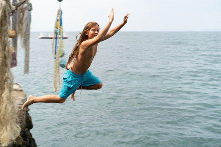 Children jump joyfully into the refreshing sea, playing by the shore on a sunny day.の写真素材