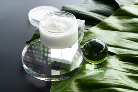 A template for cream in a transparent bottle on a black background with green tropical leaves.High angle view.の写真素材