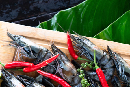 Tiger prawns are beautifully arranged on banana leaves, surrounded by fiery red chilies and green peppercorns. This vibrant display showcases the richness of Asian cuisine and local ingredients.の写真素材