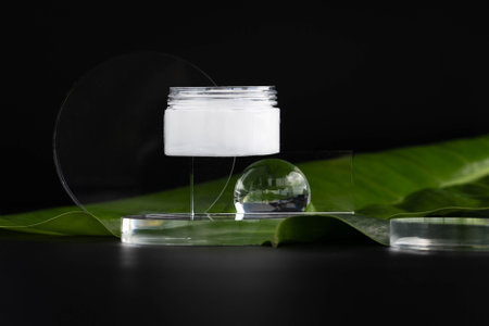Cream in a jar on a black background with elements of a glass sphere. On banana leaves. Eco-friendly concept.の写真素材