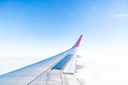 Gazing out from the cabin, a vivid view reveals the graceful curve of an aircraft wing. Lush clouds stretch endlessly below, capturing the essence of flight, adventure, and boundless freedom.の写真素材