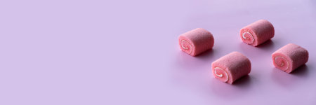 Four pink rolled pastries are arranged on a soft rose-patterned surface.の写真素材
