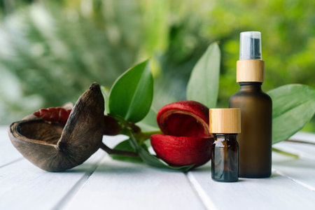 Two cosmetic bottles with pipettes placed near vibrant red petals and green leaves in a garden.の写真素材
