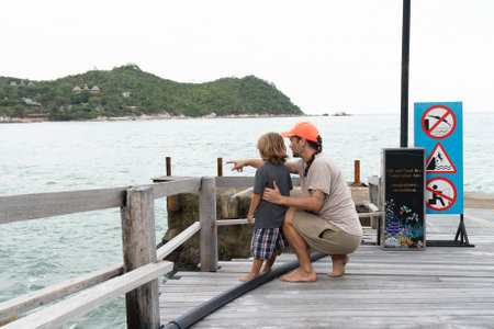 A young father at the marina shows his son at sea and explains his behavior on the beach during the journeysの写真素材