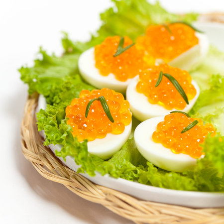 Red caviar canape with quail egg and rosemary on white macro