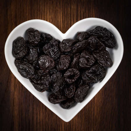Dried Plums Pitted Prunes in Heart Shaped Bowl. Selective focus.の写真素材