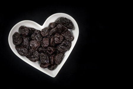 Dried Plums Pitted Prunes in Heart Shaped Bowl on a black background. Selective focus.の写真素材