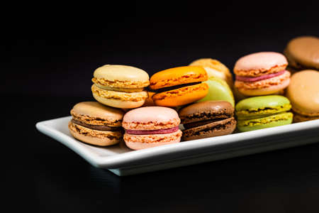 Colorful Macaroons Chocolate, Pistachio, Cherry, Orange, Vanilla Flavor Background on Black Background. Selective focus.の写真素材