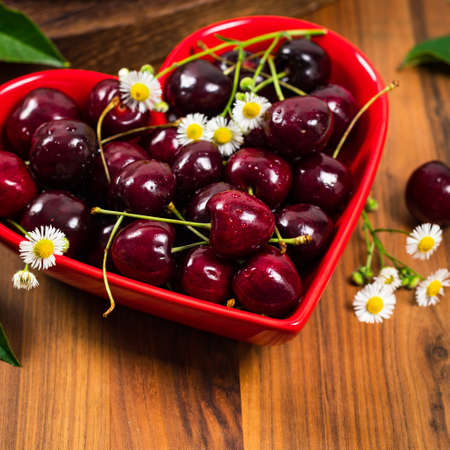Cherries in Heart Shaped Bowl on Wooden Background. Selective focus.の写真素材