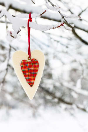 Textile Red Heart on Snowy Tree Brunch in Winter Background for Christmas and New Year Concept. Selective focus.の写真素材