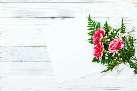 Top view of Carnation Flowers on White Vintage Wooden Background with Sheet of Paper. Design concept for Mother day, wedding and Valentine's day with copy space.の写真素材