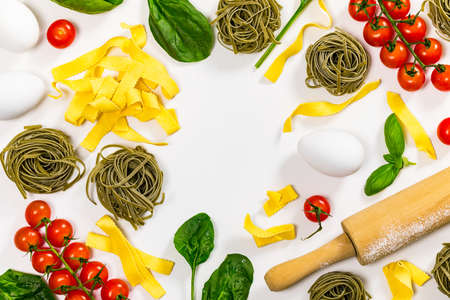 Spinach and Basil Pasta Nests with Tomatoes and Ingredients for Cooking Pasta on White Wooden Background, Italian cuisine, Top view. Selective focus.の写真素材