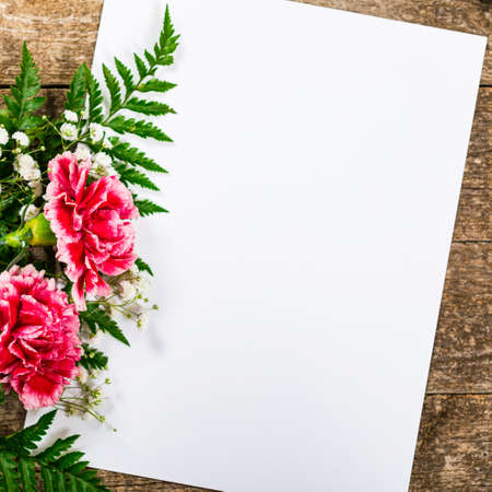 Top view of Carnation Flowers on Vintage Wooden Background with Sheet of Paper. Design concept for Mother day, wedding and Valentine's day with copy space. Selective focus.の写真素材