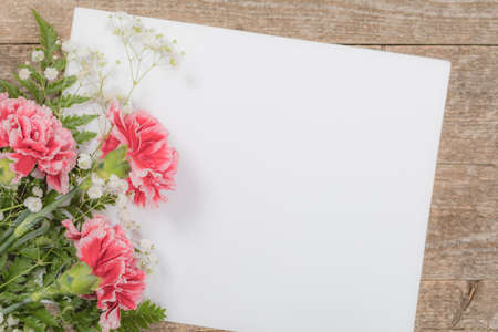 Top view of Carnation Flowers on White Vintage Wooden Background with Sheet of Paper. Design concept for Mother day, wedding and Valentine's day with copy space. Toned image. Selective focus.の写真素材