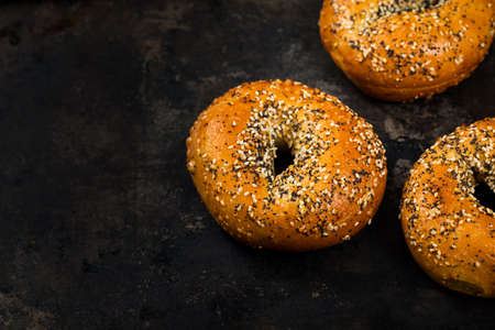 Freshly Baked Breakfast Bagels Topped with Sesame Seeds, Poppyseeds, Garlic and Onion on Old Dark Rusty Metal Background. Selective focus.の写真素材