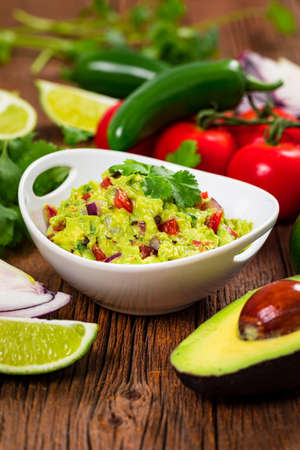 Bowl of Guacamole next to Fresh Ingredients on a Table with Tortilla Chips. Selective focus.の写真素材