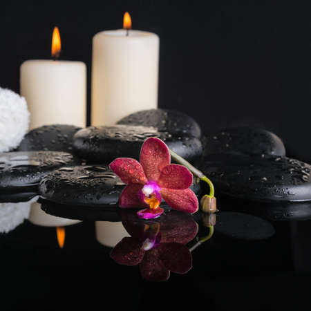 Beautiful spa concept of zen stones with drops, purple orchid (phalaenopsis), candles with reflection on water, white towelsの写真素材