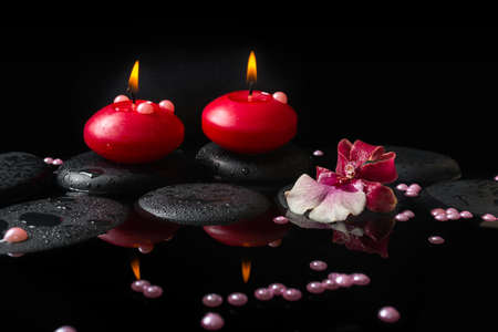 Beautiful spa concept of white and red orchid (cambria), red candles and pearl beads on zen stones with drops, reflection waterの写真素材