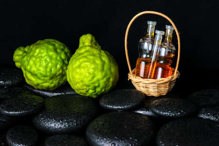 Aromatic spa concept of bottles essential oil in basket, bergamot and zen basalt stones with dew on black background, closeupの写真素材