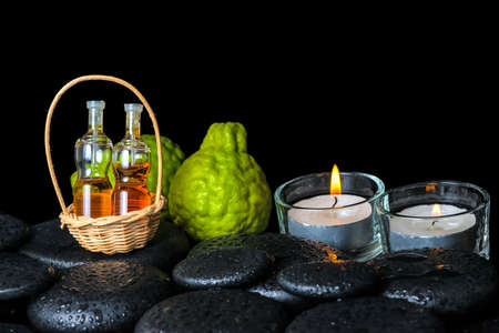 Aromatic spa concept of bergamot fruits, candles and bottles essential oil in basket on zen black stones with dew, closeupの写真素材
