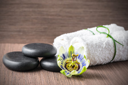 beautiful spa concept of passiflora flower, black zen stones and white towels on wooden background, closeupの写真素材