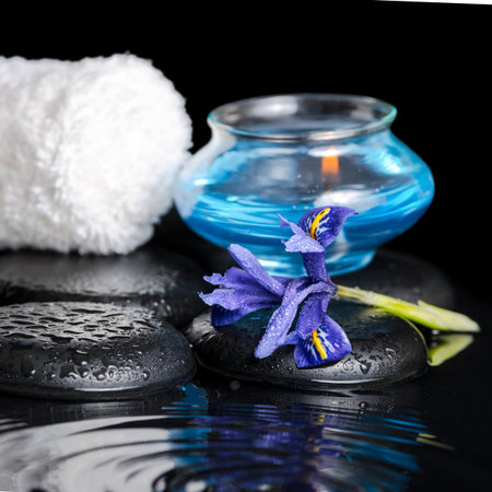 beautiful spa concept of iris flower, blue candle, white towel and black zen stones on ripple reflection water, closeupの写真素材