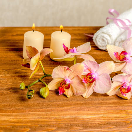 beautiful spa concept of blooming twig orchid flower, phalaenopsis, white towels and candles on wooden background, closeupの写真素材