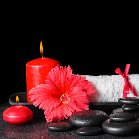 beautiful spa concept of red hibiscus flower with dew, candles and white rolled towel tied with a ribbon on zen stones, closeupの写真素材
