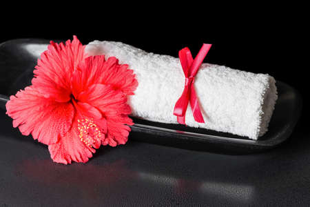beautiful spa concept of red hibiscus flower with dew and white rolled towel tied with a ribbon, closeupの写真素材