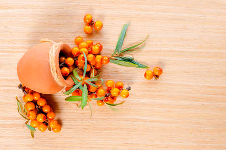 berries are scattered out of a ceramic pot on a wooden backgroundの写真素材