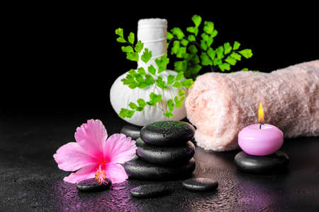 beautiful spa still life of pink hibiscus flower, leaf fern, thai herbal compress ball, towel, candle and stones with dew, closeupの写真素材