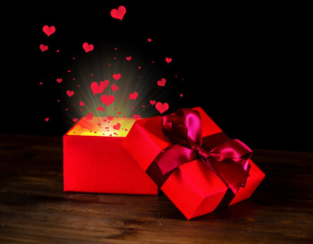 greeting opened box with bow and miracle light on wooden background is isolated on black, closeupの写真素材