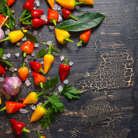 top down of yellow, red hot chili peppers, sea salt, greenery, black peppers and garlic on cracks black background, close upの写真素材