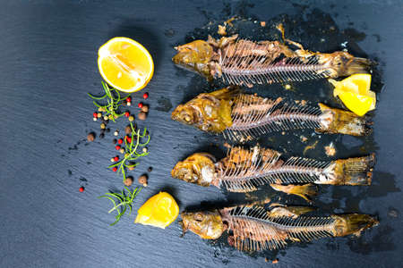 top view of fish skeleton bones, squeezed lemon and flavor peppers on slate background, close upの写真素材