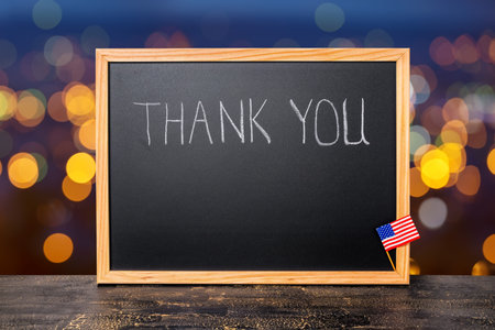 handwriting text thank you is written in chalkboard with flag on city light background and...