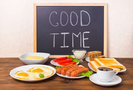 concept breakfast with handwritten text good time on blackboard with setting food products over wooden backgroundの写真素材