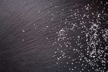 sprinkled sea salt over black slate stone background, top viewの写真素材