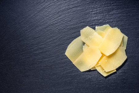 top view of tasty fresh yellow thin slice parm cheese on black stone slate background, close up の写真素材