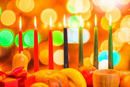 african Kwanzaa festive concept with decorate seven candles red, black and green, gift box, pumpkin, bowl and fruit on light blur bokeh background, close upの写真素材
